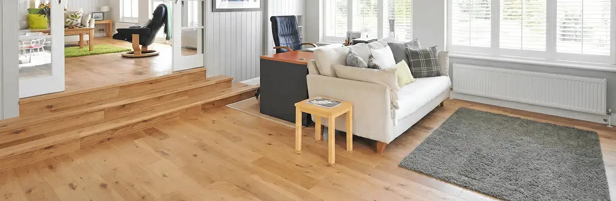 A modern living room with professionally installed laminate flooring, a beige sofa, a small side table, a gray rug, and large windows with white shutters in Bellevue, WA